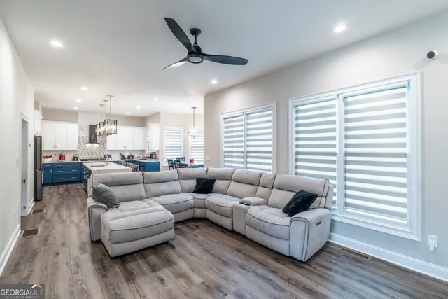 a kitchen with stainless steel appliances granite countertop a sink dishwasher a stove a refrigerator a kitchen island and couches with wooden floor