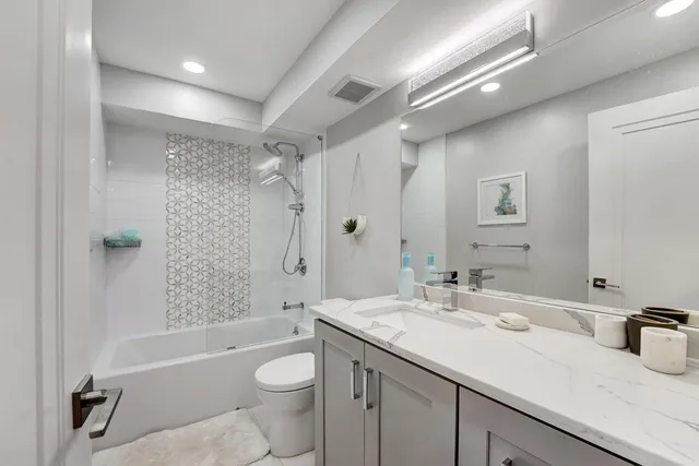 a bathroom with a granite countertop sink a toilet a mirror a bathtub and shower