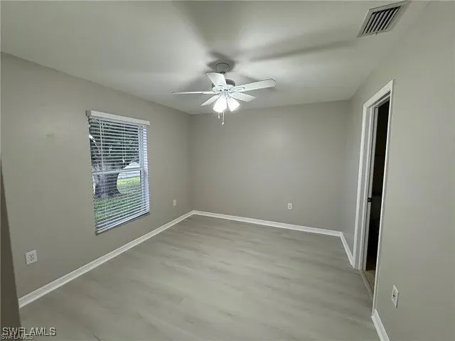 an empty room with chandelier fan and windows