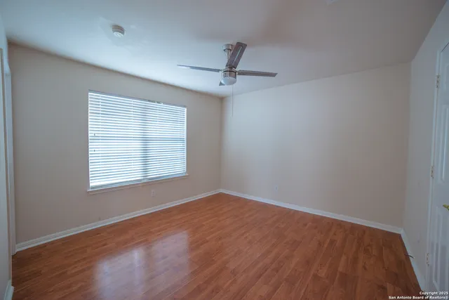 an empty room with wooden floor ceiling fan and windows