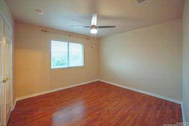 an empty room with wooden floor ceiling fan and windows