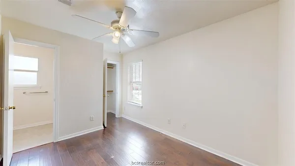 an empty room with wooden floor fan and windows