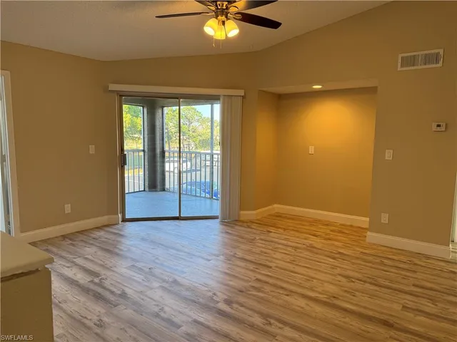 a view of an empty room with wooden floor and a ceiling fan