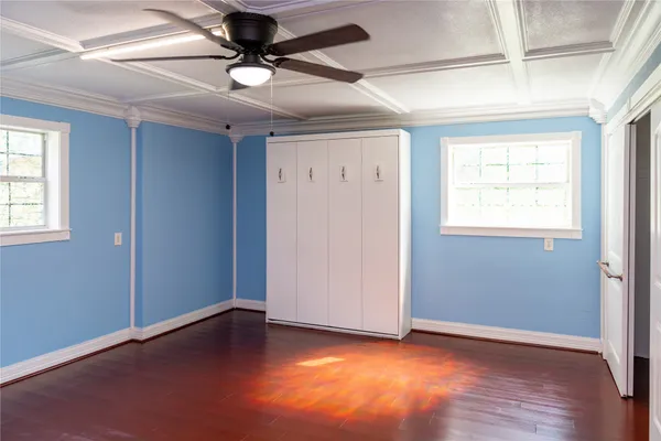 an empty room with wooden floor chandelier fan and windows