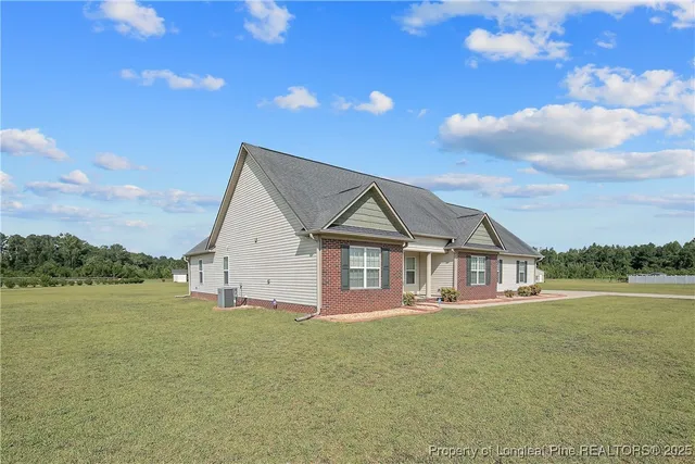 a view of a house next to a big yard with plants and large tree