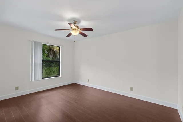 an empty room with wooden floor ceiling fan with window