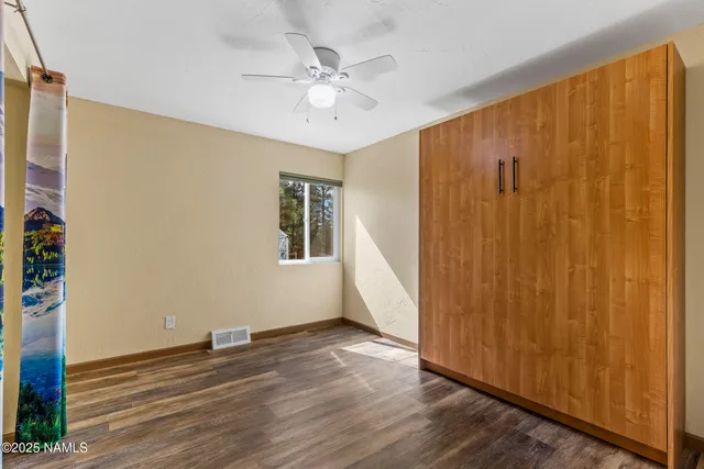 an empty room with wooden floor fan and windows