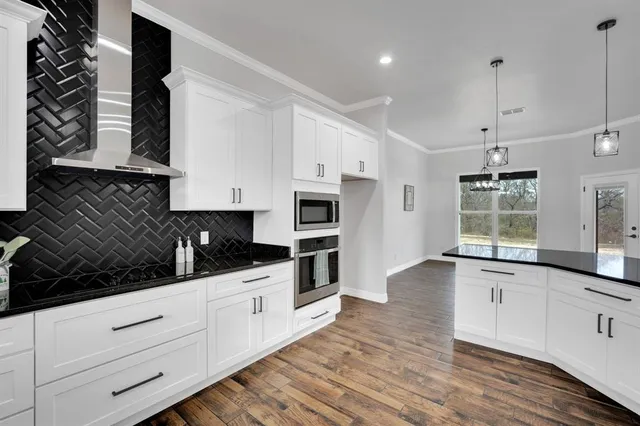 a kitchen with stainless steel appliances kitchen island granite countertop a stove a sink and white cabinets with wooden floor