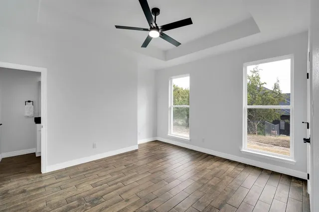 an empty room with wooden floor fan and windows