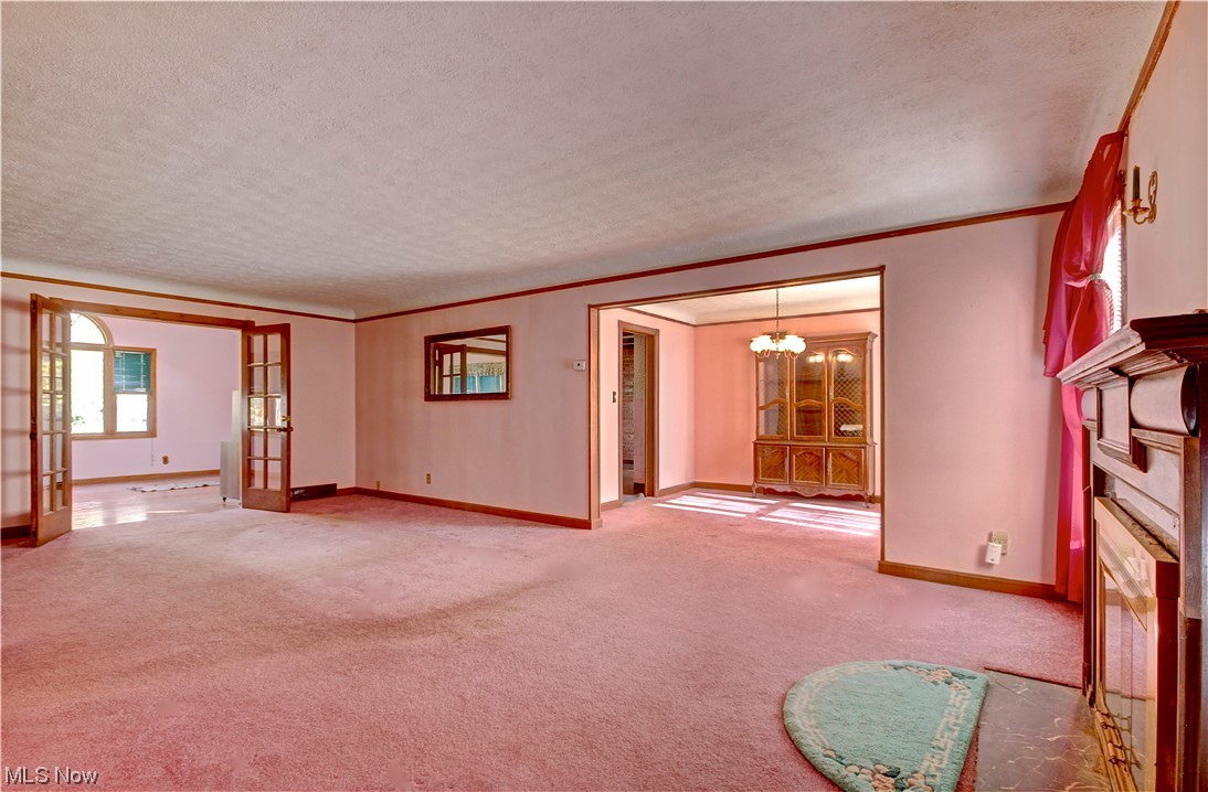 20930 Eaton Road Cleveland, OH 44126 - Photo 6 of 33 Unfurnished living room featuring a fireplace, french doors, a chandelier, ornamental molding, and light carpet