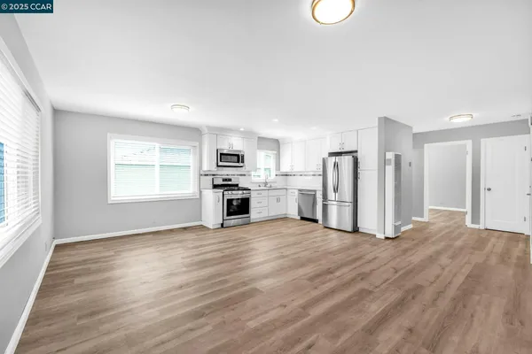 a kitchen with granite countertop a refrigerator a stove a sink and white cabinets with wooden floor