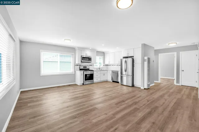 a kitchen with granite countertop a refrigerator a stove a sink and white cabinets with wooden floor