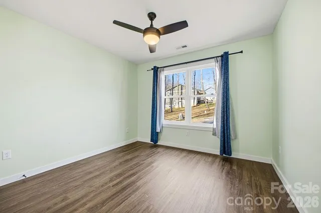 an empty room with wooden floor chandelier fan and windows