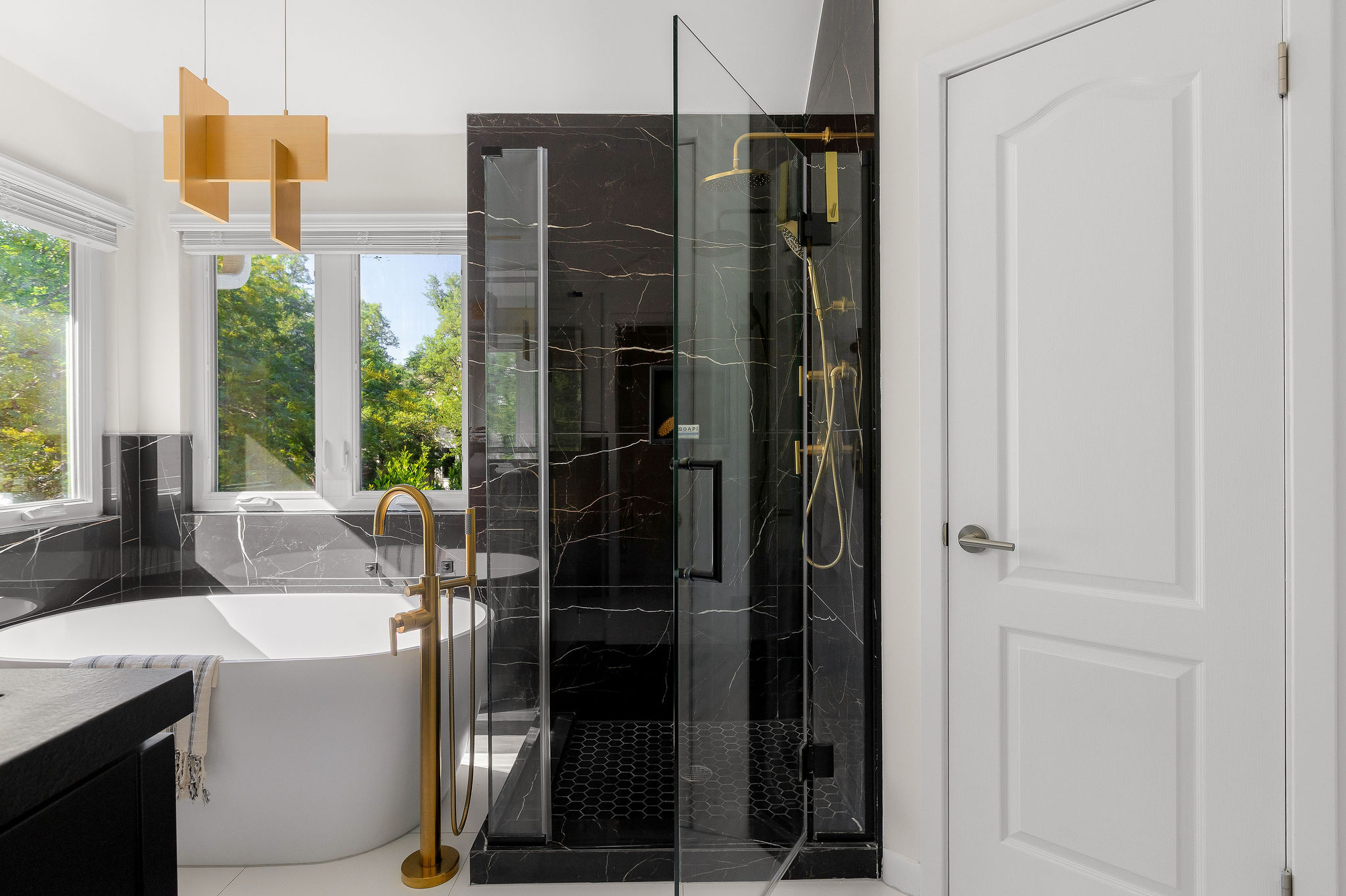 6500 Clay Allison Pass Austin, TX 78749 - Photo 25 of 39 Freestanding soaking tub with a floor-mounted gold-tone faucet, complemented by a glass-enclosed shower featuring black marble-style tile and gold-tone fixtures