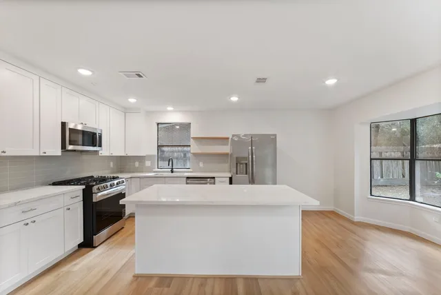 a kitchen with stainless steel appliances kitchen island granite countertop a stove a sink a refrigerator and white cabinets with wooden floor