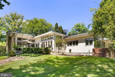 a view of a white house with a big yard and potted plants and large trees