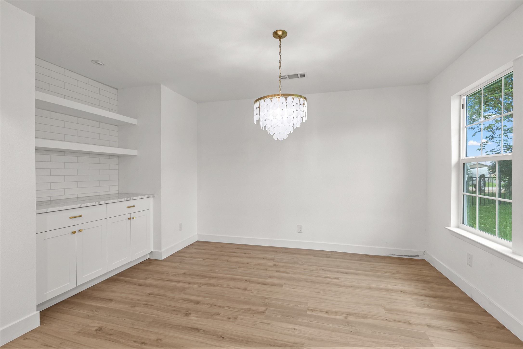 409 Ave R Marble Falls, TX 78654 - Photo 6 of 25 Spacious room featuring wood-finish flooring, a contemporary chandelier, and a built-in cabinet with a subway tile backsplash and floating shelves