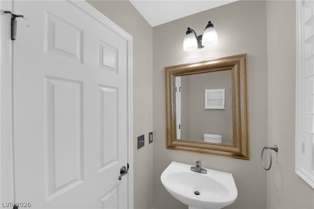 646 Monument Point Street Henderson, NV 89002 - Photo 7 of 44 A compact powder room with pedestal sink and decorative mirror provides essential convenience.