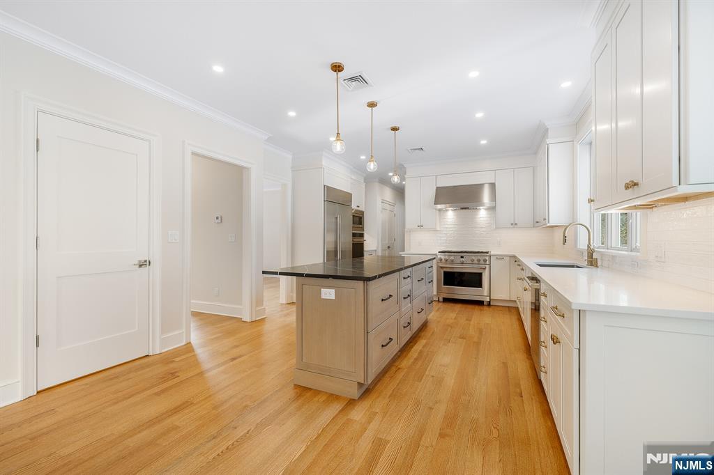 62 Colony Avenue Park Ridge, NJ 07656 - Photo 11 of 50 a large kitchen with kitchen island a stove a sink a refrigerator and white cabinets with wooden floor