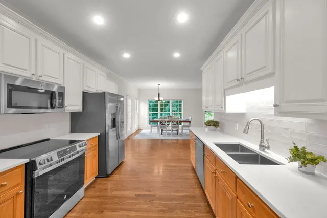 a kitchen with stainless steel appliances a sink dishwasher a stove top oven a refrigerator with wooden cabinets and floor