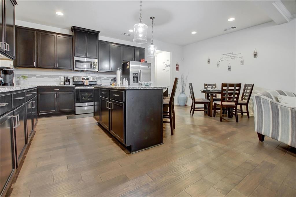7687 Cabrini Place Fairburn, GA 30213 - Photo 7 of 29 a kitchen with stainless steel appliances granite countertop a stove top oven a sink a dining table and chairs