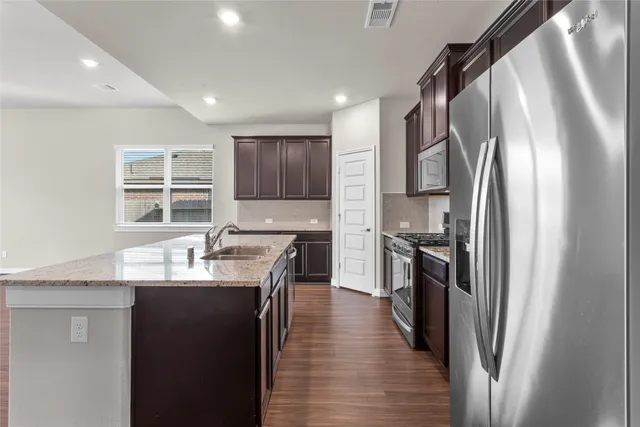 a kitchen with stainless steel appliances granite countertop a refrigerator a sink dishwasher a stove and a dining table with wooden floor