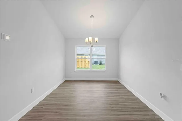 an empty room with wooden floor chandelier and windows
