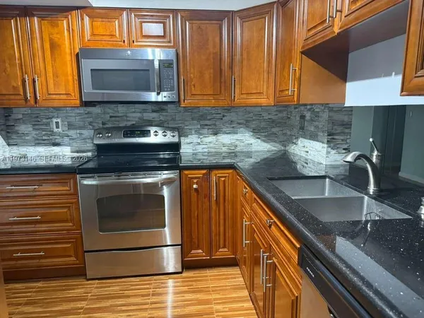 a kitchen with granite countertop a stove top oven cabinetry a sink and a microwave