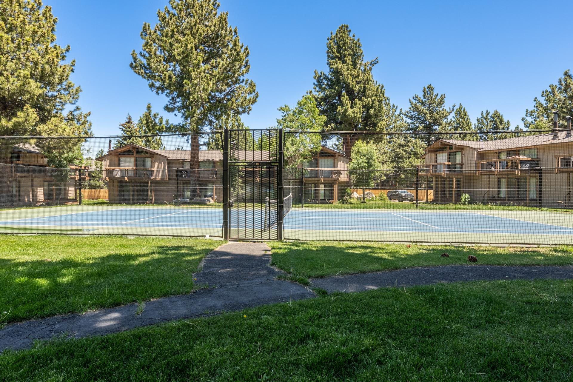 3252 Chateau Road, Unit 43 Mammoth Lakes, CA 93546 - Photo 27 of 29 Tennis court featuring a blue playing surface and green surrounds, enclosed by a black chain-link fence with a gate