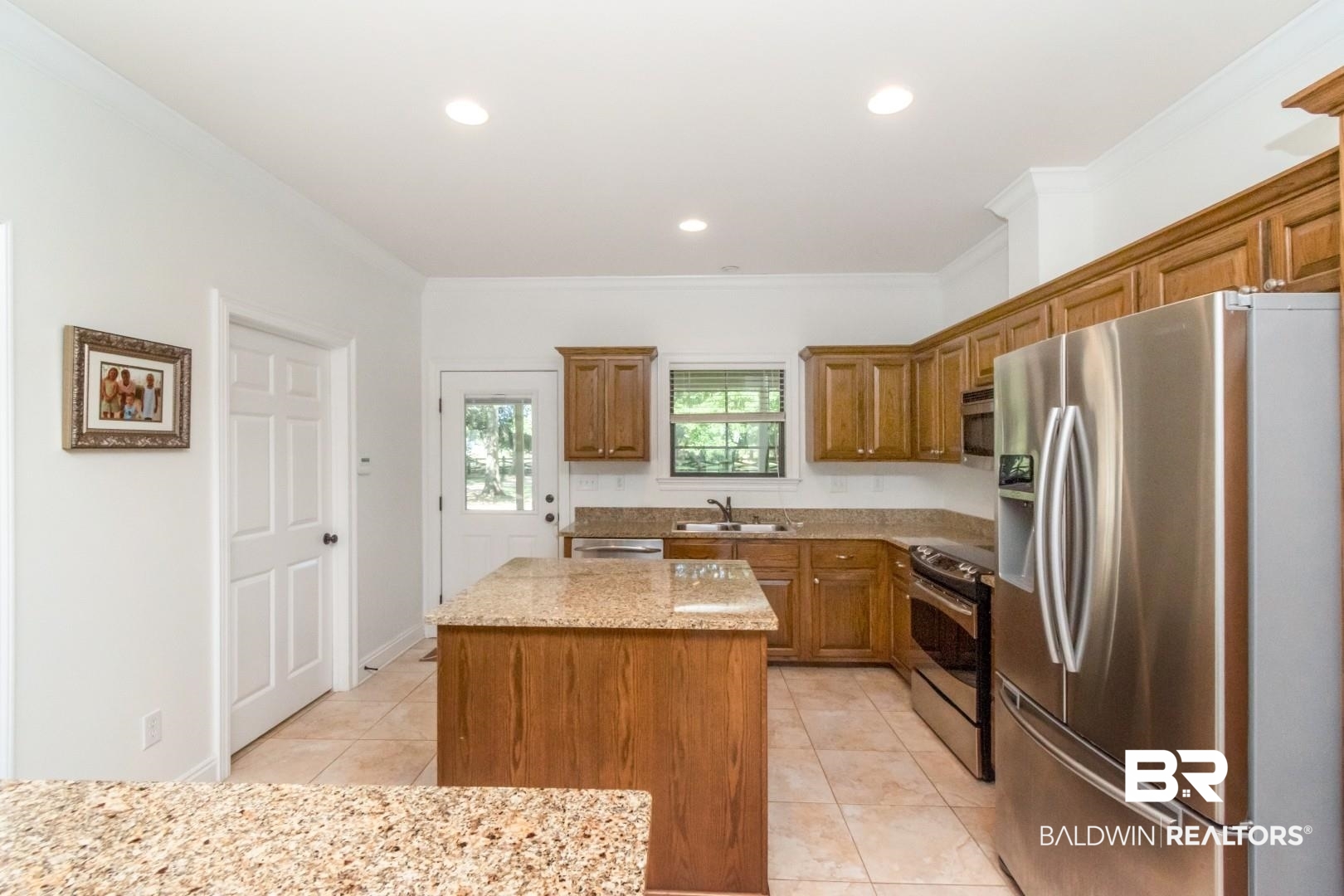 1360 Dykes Road North Mobile, AL 36608 - Photo 9 of 40 Kitchen with appliances with stainless steel finishes, crown molding, brown cabinetry, a kitchen island, and light tile patterned floors
