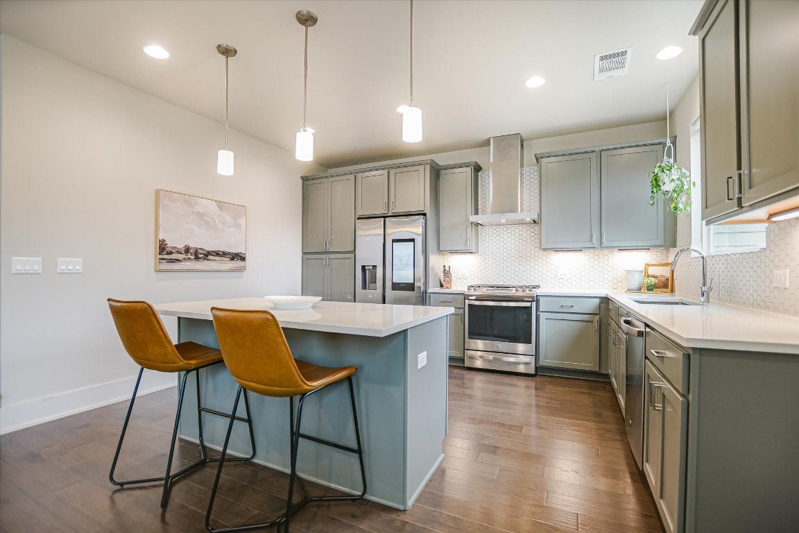 5212 Pink Poppy Pass, Unit 20 Austin, TX 78735 - Photo 10 of 24 Kitchen with appliances with stainless steel finishes, wall chimney exhaust hood, a center island, hanging light fixtures, and a kitchen breakfast bar