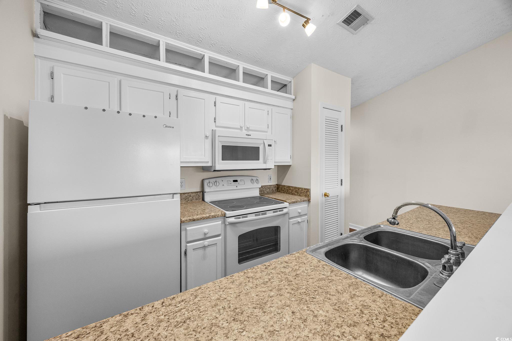 673 Tupelo Lane, Unit 19H Longs, SC 29568 - Photo 9 of 22 Kitchen featuring white appliances, light countertops, white cabinets, a textured ceiling, and rail lighting