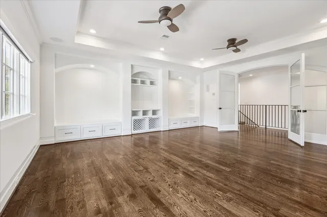 an empty room with wooden floor ceiling fan and windows