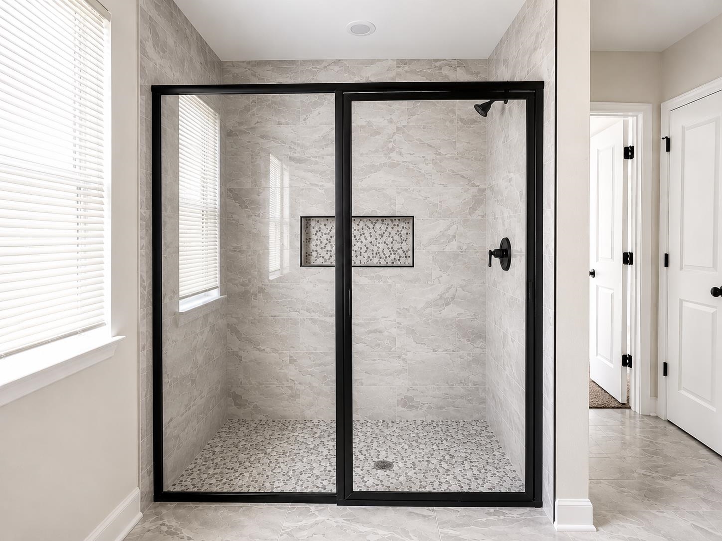 1687 East Alcy Road Memphis, TN 38114 - Photo 6 of 7 Walk-in shower featuring a matte black framed glass enclosure, light-toned stone-finish tile walls, and a pebble-finish shower pan