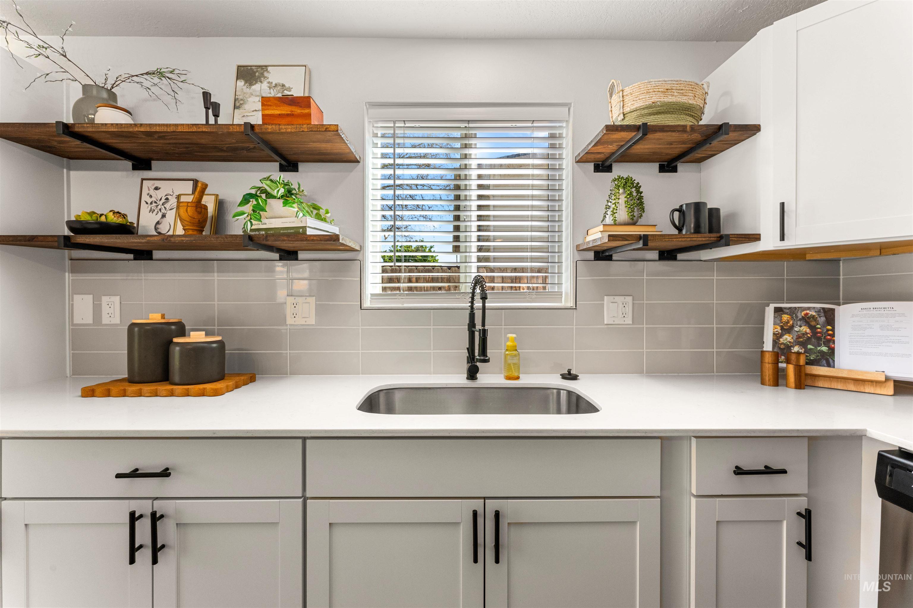 4700 Jennifer Street Boise, ID 83704 - Photo 13 of 39 Kitchen featuring a stainless steel undermount sink with a matte black faucet, light grey subway tile backsplash, white shaker-style cabinetry with black hardware, and open wood-finish shelving