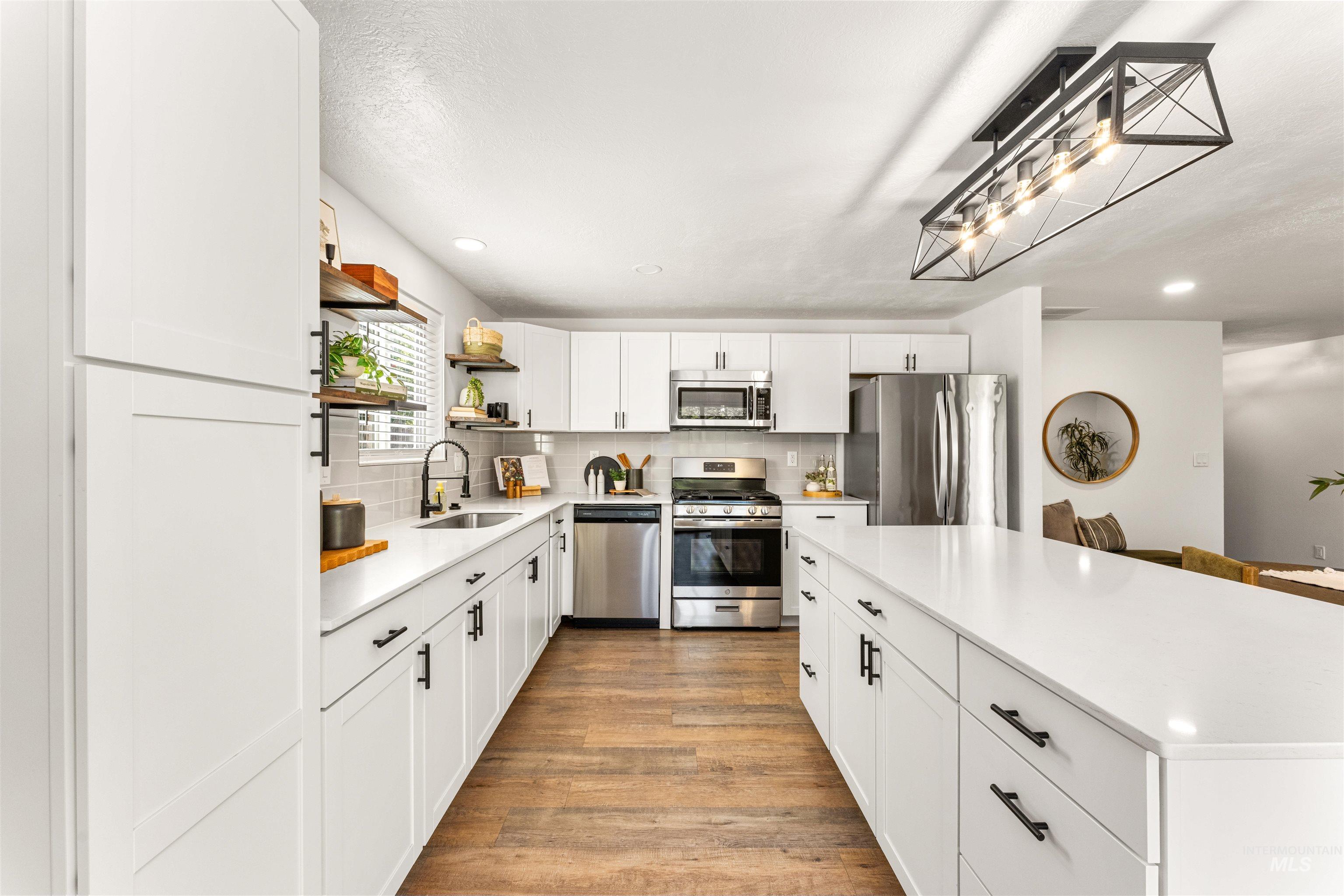 4700 Jennifer Street Boise, ID 83704 - Photo 15 of 39 Bright kitchen featuring white shaker cabinetry, stainless steel appliances, a center island with countertop seating, wood-finish flooring, and a linear pendant light fixture