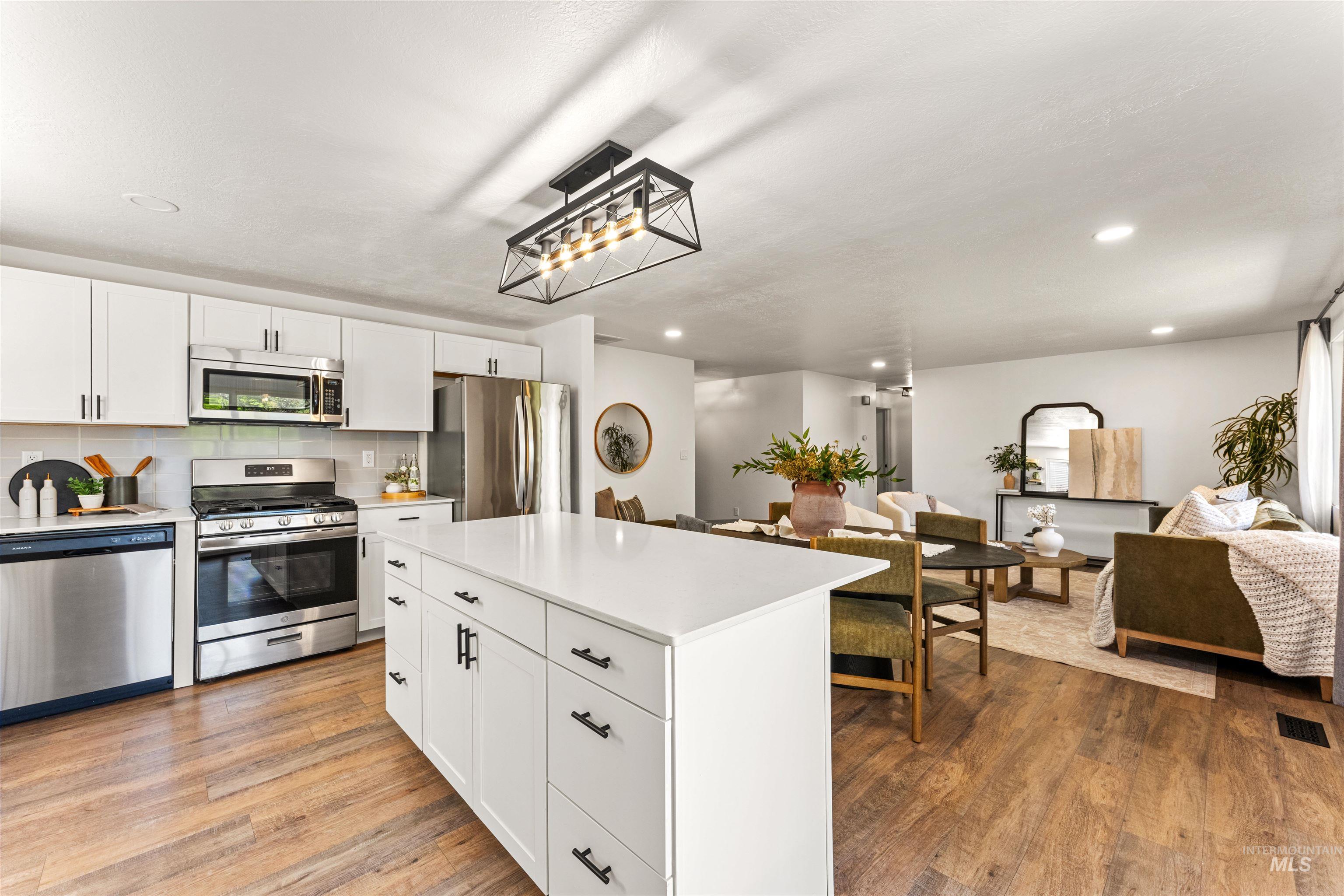 4700 Jennifer Street Boise, ID 83704 - Photo 17 of 39 Open-concept living area featuring a kitchen with white cabinetry, stainless steel appliances, a center island with a white countertop, and wood-finish flooring extending throughout