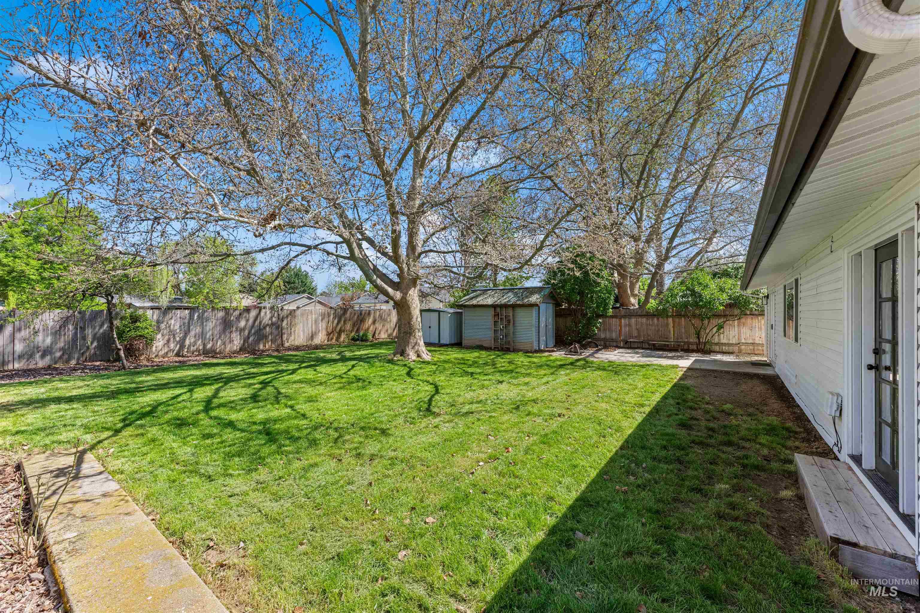 4700 Jennifer Street Boise, ID 83704 - Photo 30 of 39 Expansive grassy yard featuring a prominent mature tree, privacy fencing, and two storage sheds
