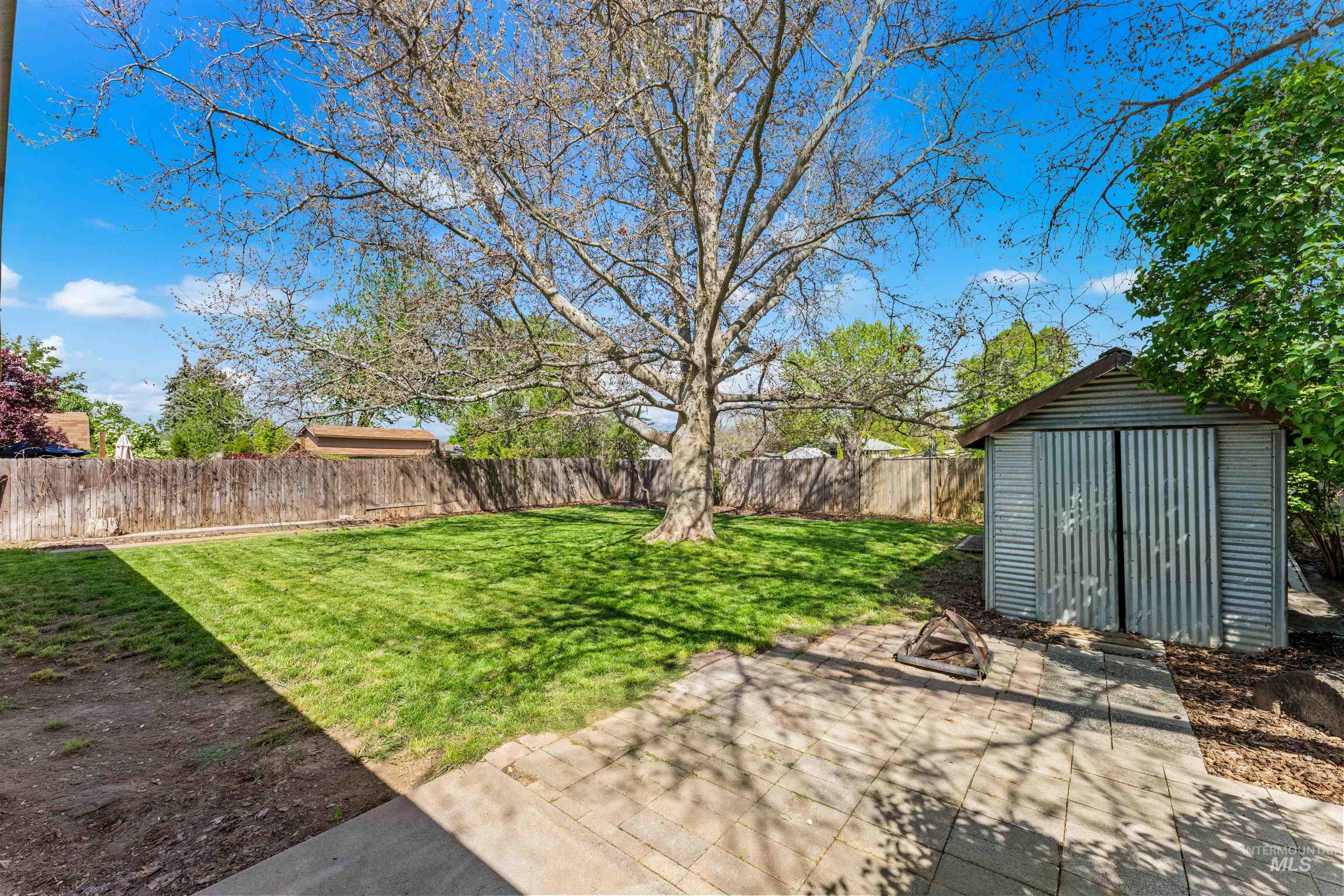 4700 Jennifer Street Boise, ID 83704 - Photo 31 of 39 Expansive backyard featuring a large mature tree, a corrugated metal shed, a wood fence perimeter, a paver patio area, and a lush green lawn