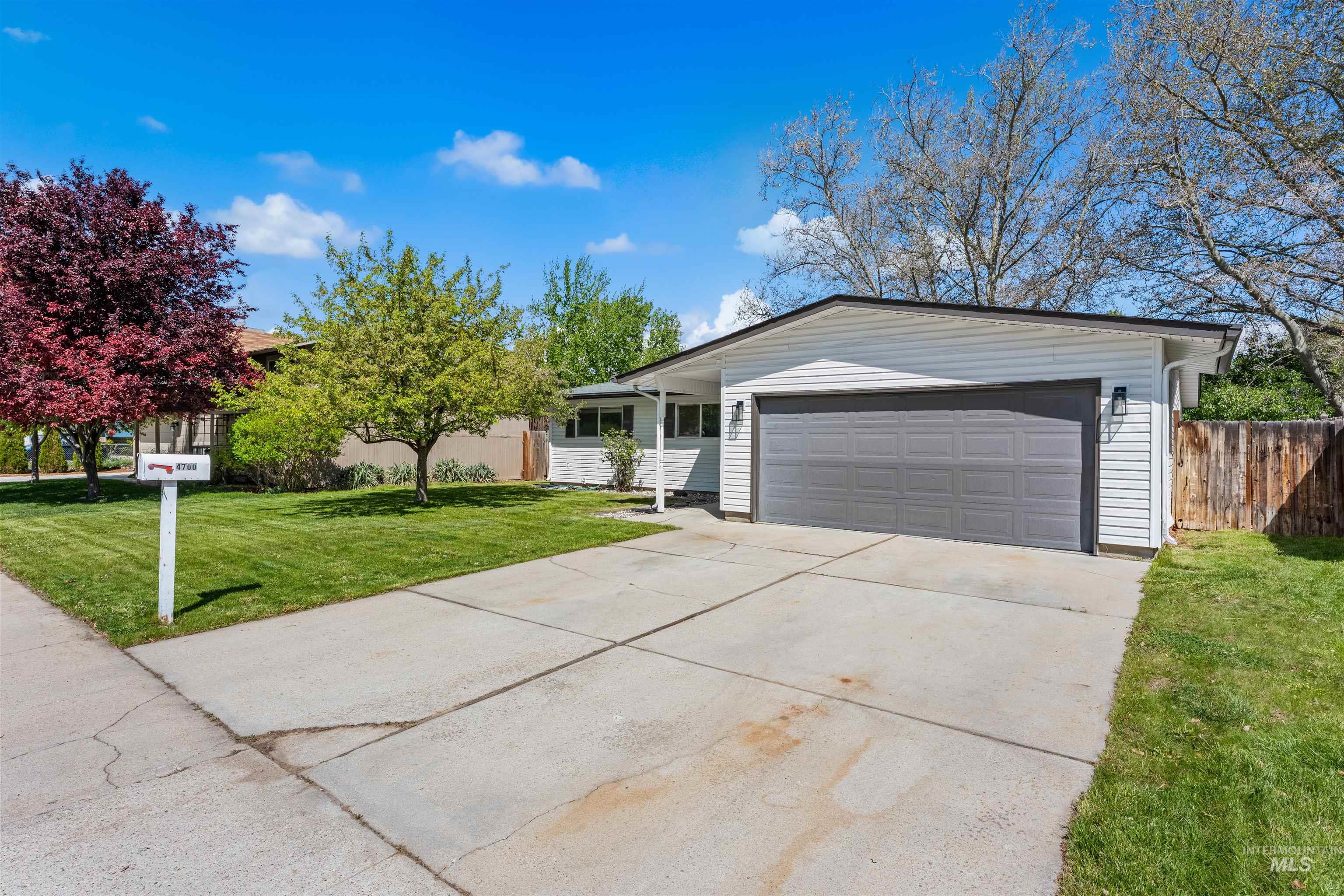 4700 Jennifer Street Boise, ID 83704 - Photo 39 of 39 White siding exterior with a dark-toned garage door, mature front yard trees, concrete driveway, and a wood privacy fence