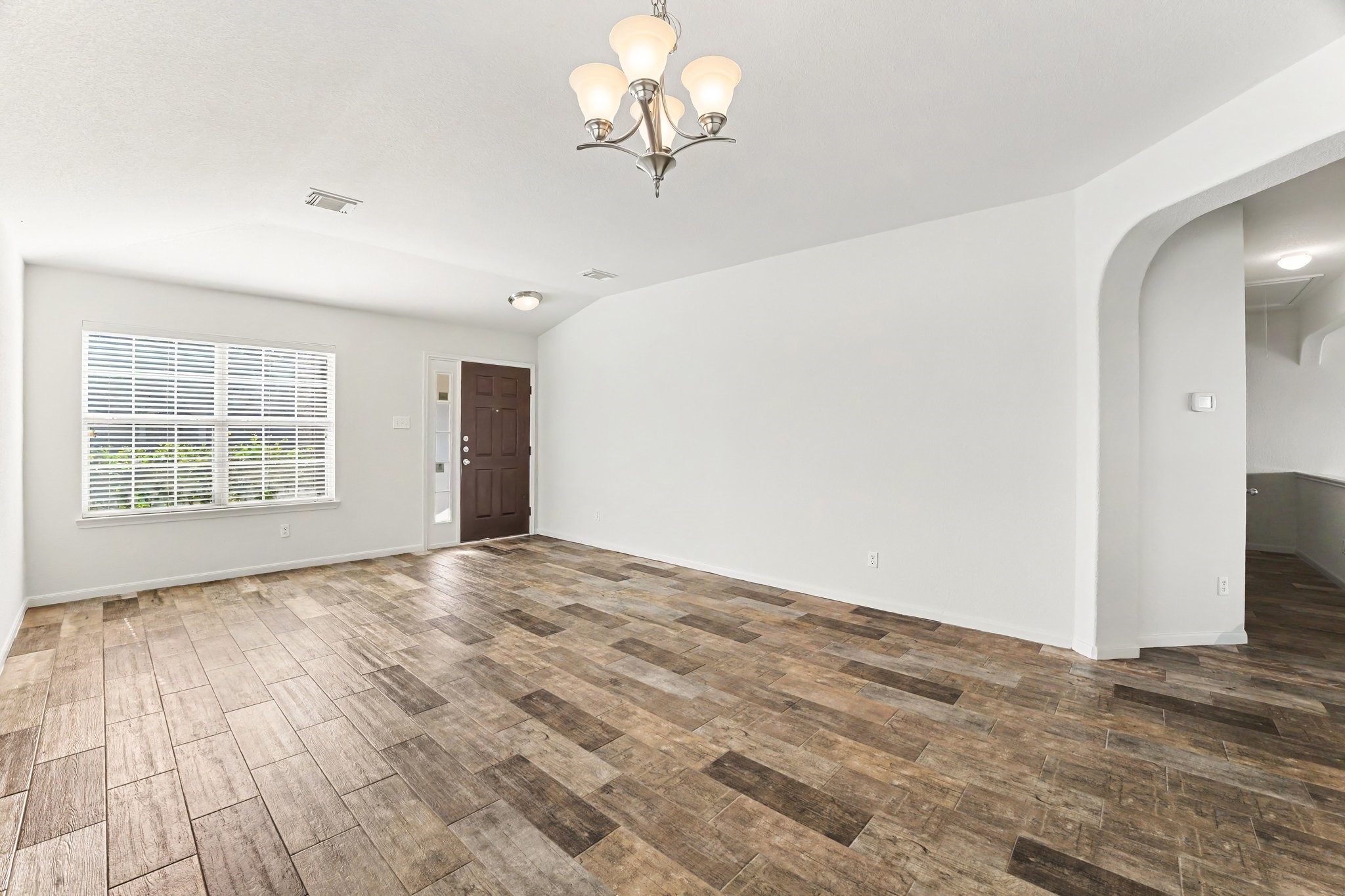 21427 Blooming Rock Lane Spring, TX 77379 - Photo 5 of 32 This spacious room features a modern wood-look tile floor, neutral walls, and ample natural light from a large window. The entryway has a dark wooden door, and there's an elegant light fixture on the ceiling, creating a welcoming atmosphere.