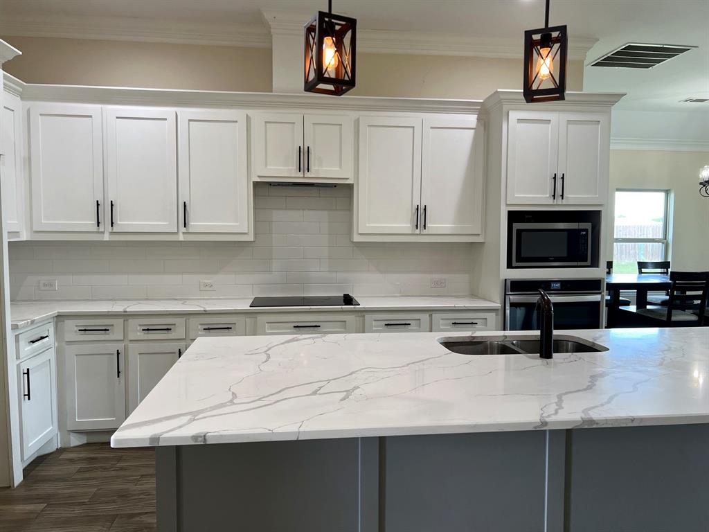 8008 County Road 1058 Rice, TX 75155 - Photo 4 of 12 Kitchen with white shaker cabinetry, white subway tile backsplash, white countertops with grey veining, and a central island with an undermount sink