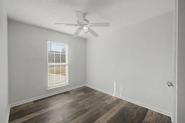 an empty room with wooden floor fan and windows