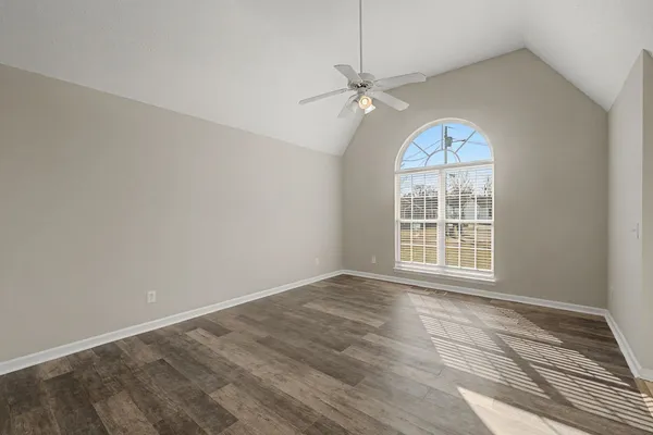 an empty room with wooden floor fan and windows