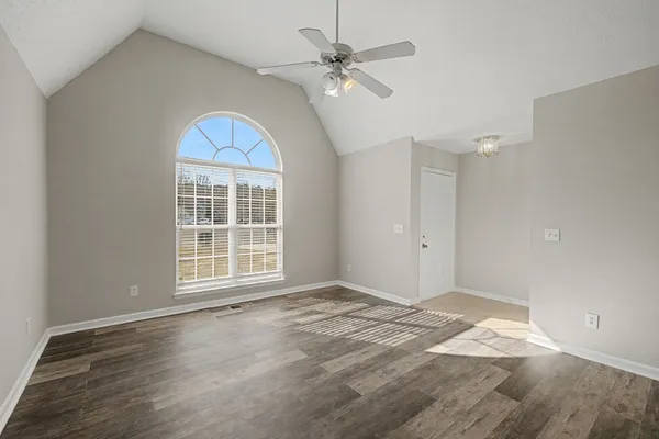 an empty room with wooden floor chandelier fan and windows