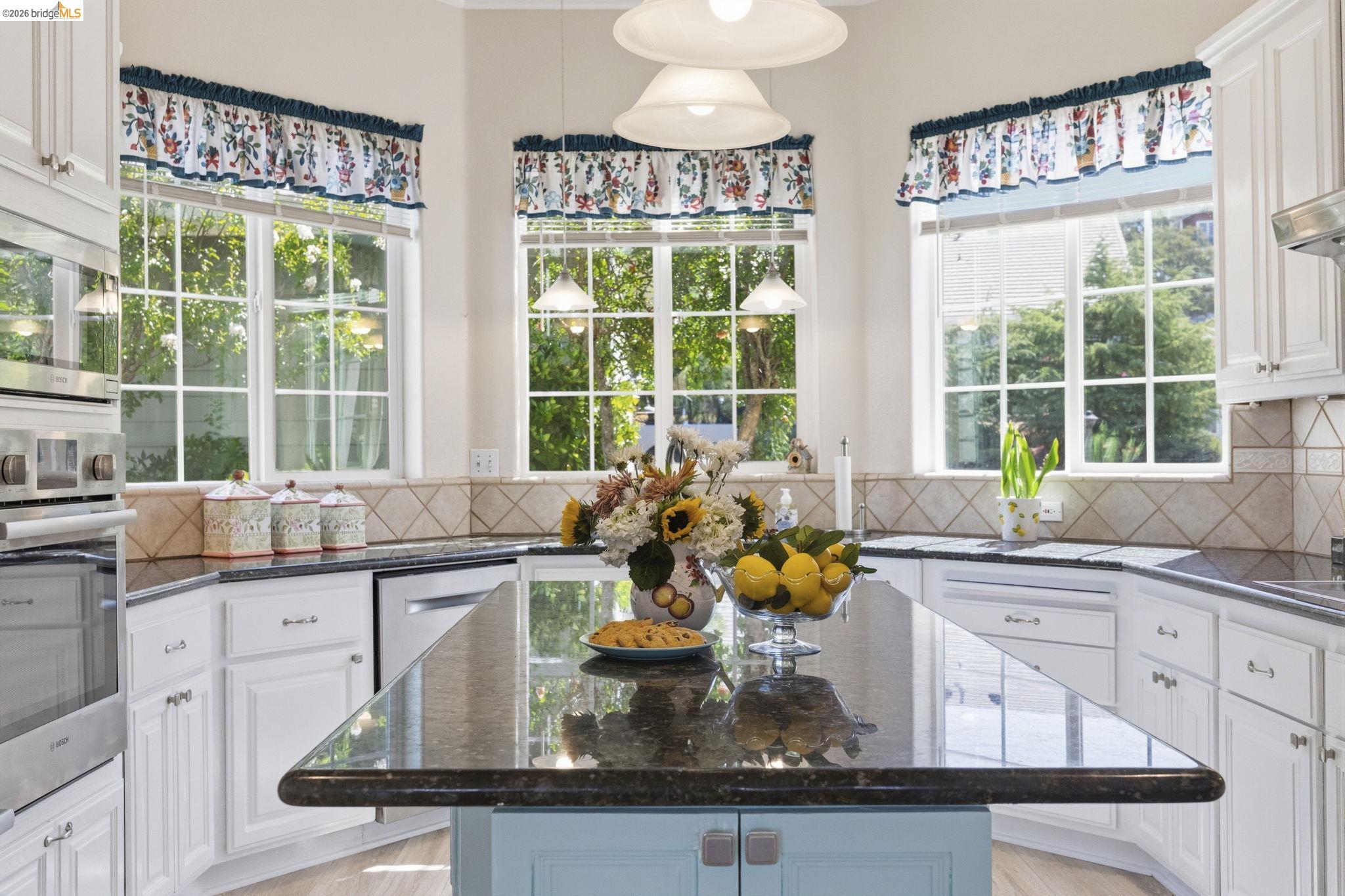 6242 Bluff View Road Copperopolis, CA 95228 - Photo 18 of 59 Kitchen featuring a central island with a dark granite countertop, white cabinetry, integrated stainless steel Bosch appliances, and multiple windows for great natural light overlooking the flowering trees