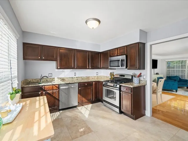 a kitchen with stainless steel appliances granite countertop a stove top oven a sink dishwasher a dining table and chairs with wooden floor