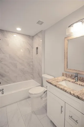 a bathroom with a granite countertop sink a toilet a mirror and bathtub