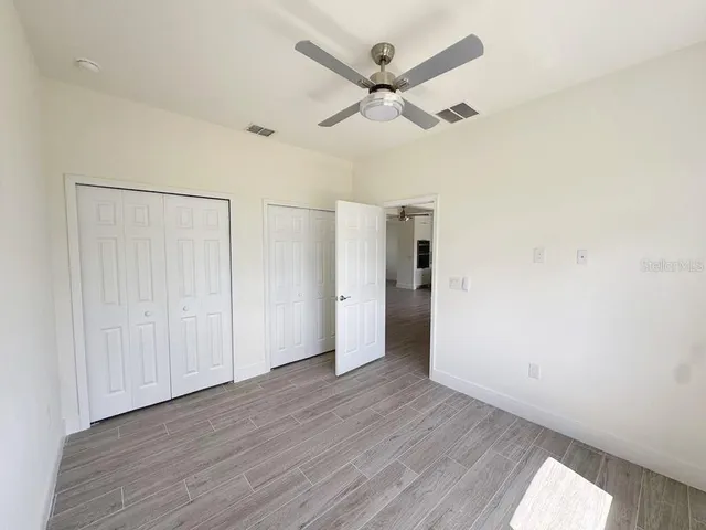 an empty room with wooden floor ceiling fan and windows