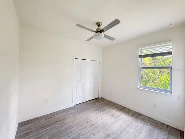 an empty room with wooden floor ceiling fan and windows